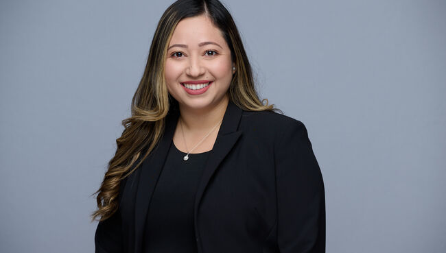 flor smiling with black shirt and blazer in front of gray background