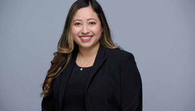 flor smiling with black shirt and blazer in front of gray background