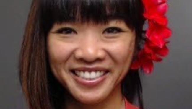 Esther Guerpo smiling in a headshot photo with a red shirt and red flower in hahir