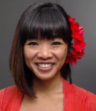 Esther Guerpo smiling in a headshot photo with a red shirt and red flower in hahir